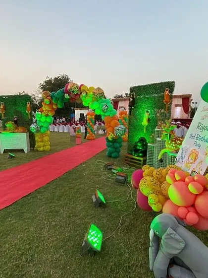 The grand entrance to Riyaan's 3rd birthday party, with a red carpet leading through a path of green hedge walls and colorful, animal-print balloon arrangements.