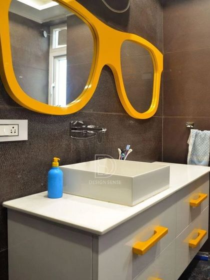 A fun and quirky kids' bathroom from the Casa Savera project. The standout feature is the large, glasses-shaped mirror in bright yellow, paired with matching yellow handles on the vanity.