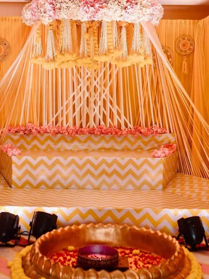 The full setup for the Haldi ceremony, showing the tiered stage with chevron patterns and the central lotus tub.