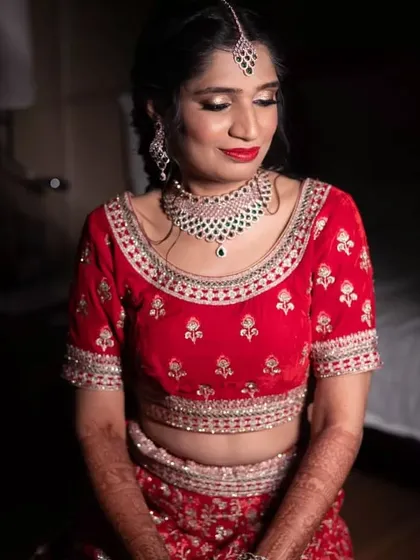 A serene portrait of the bride before her Sangeet. The dramatic lighting highlights her golden eyeshadow and bold red lipstick.