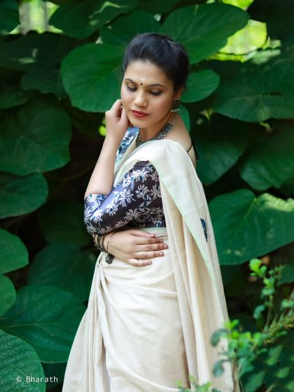 A thoughtful and serene portrait, with the subject surrounded by giant green leaves that complement her traditional attire.
