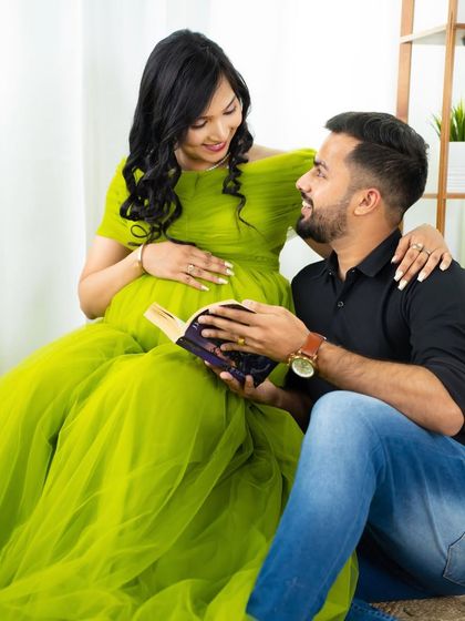 A sweet moment of shared reading. The dad-to-be holds a book while looking lovingly at his partner, who is radiant in a bright green gown.