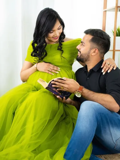 A sweet moment of shared reading. The dad-to-be holds a book while looking lovingly at his partner, who is radiant in a bright green gown.
