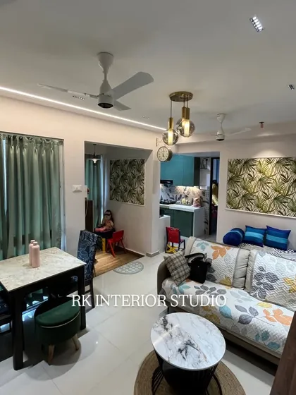 A wider angle of the living room, showing the compact dining table setup and the open flow into the kitchen. The use of matching wallpaper panels creates a sense of continuity in the design.