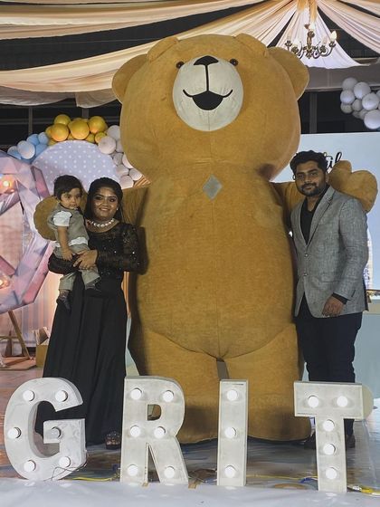 A family poses with our brown Teddy Bear at a first birthday party. Our mascots are a great way to add a special touch to your family milestone photos.