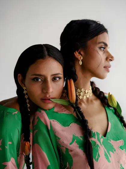 An intimate dual portrait for Esha Arora. The composition is soft and romantic, focusing on the models' connection and the details of their hair, jewelry, and printed garments.