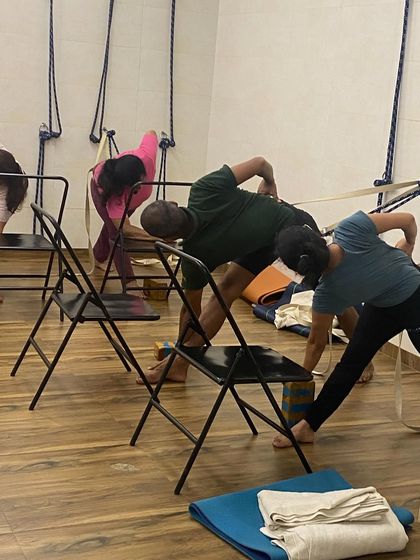 Students practicing Parivrtta Trikonasana (Revolved Triangle Pose) with chairs and blocks. The props help to elevate the torso and facilitate a deeper twist.
