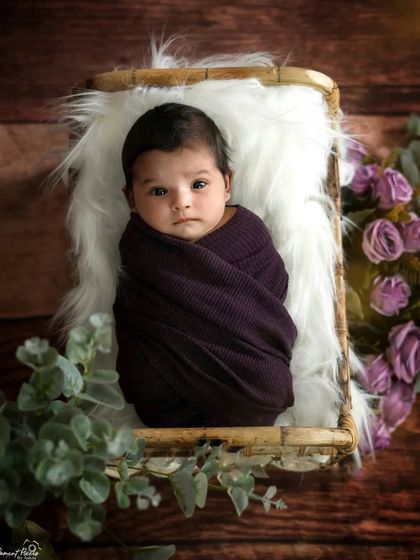 A curious newborn wrapped in a cozy purple swaddle. Her wide eyes and alert expression are just as precious as the sleepy shots.
