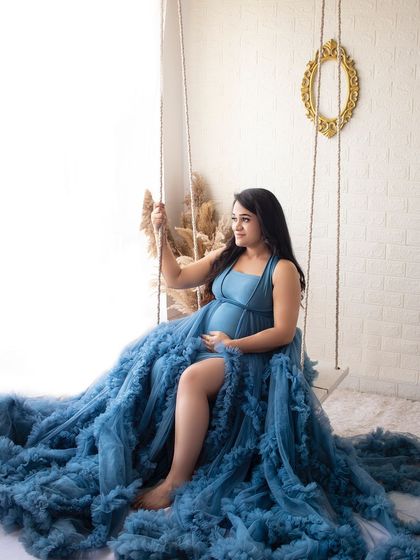 A serene portrait of a mother-to-be on the studio swing, surrounded by the flowing fabric of her deep blue gown.