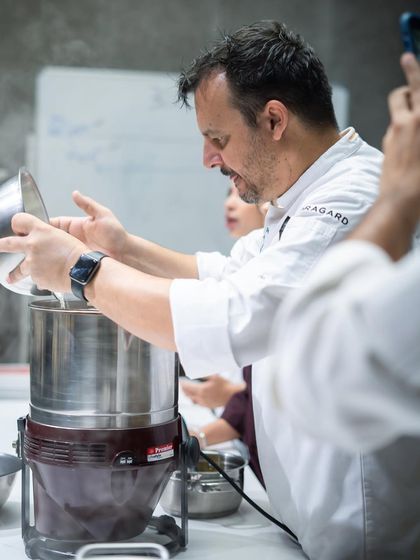 A chef demonstrates how to load roasted cacao nibs into a grinder, a key step in creating smooth, refined chocolate liquor.