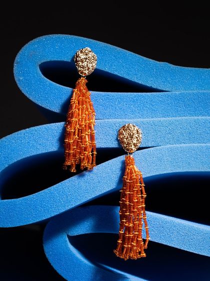 Orange tassel earrings set against a textured blue foam background. The complementary colors and interesting textures make this shot stand out.