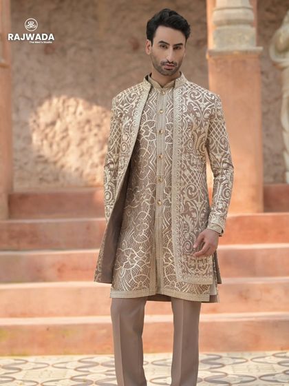A full-length view of the beige embroidered Indo-Western outfit. The long jacket with its intricate patterns is the centerpiece of this regal ensemble from the Riwayat collection.
