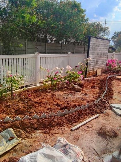 The initial stages of a garden makeover. Here, our team is preparing the soil and defining the borders for flowerbeds along a new white picket fence, laying the foundation for a colorful and structured garden design.