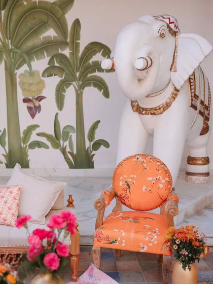 A corner of the "Ghar ka Aangan" themed welcome lunch, featuring a hand-painted wall mural and a floral-upholstered chair next to a life-sized elephant statue. This decor blended tradition with artistic flair.