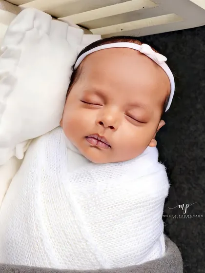 A close-up of a baby sleeping in a miniature bed, swaddled in a white wrap.