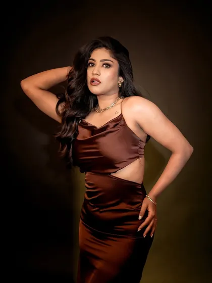 A studio portrait that captures the model's confident and powerful presence. The lighting highlights her features and the texture of her dress against a simple dark background.