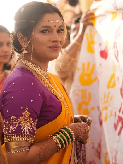 A candid shot of a bride during her wedding ceremony, wearing a yellow and purple saree. Her makeup is fresh and natural, perfect for a day event.