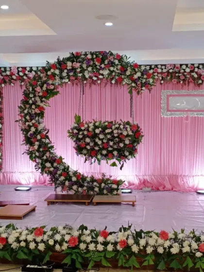 A unique crescent-shaped floral arrangement for a naming ceremony. The cradle is designed to look like it's hanging from the moon, decorated with pink, white, and red flowers for a magical touch.