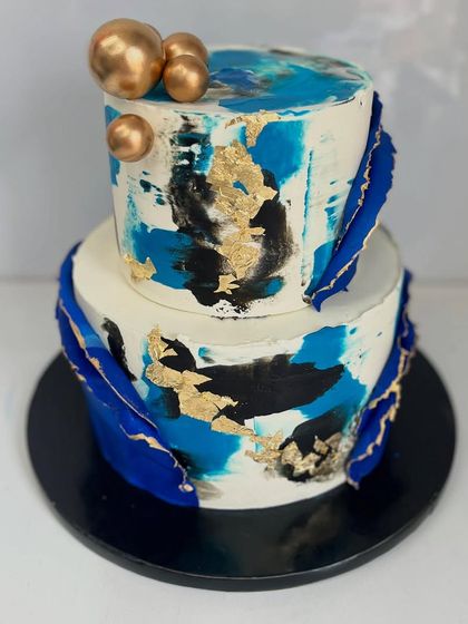 Bold, modern, and unforgettable. This two-tiered abstract cake is hand-painted with shades of deep blue and black, accented with edible gold leaf and dramatic blue sails.