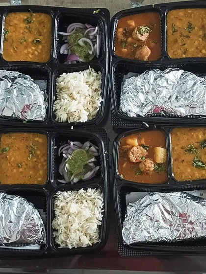 A side-by-side view of two different thali combinations. One has Jeera Aloo and Dal Tadka, while the other features a Soya Aloo curry with the same dal.