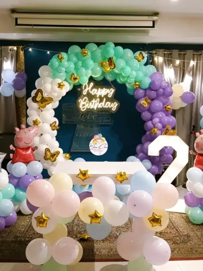 A delightful Peppa Pig themed birthday party for a second birthday. The decor includes a pastel balloon arch with butterfly accents, character foils, and a light-up number '2'.