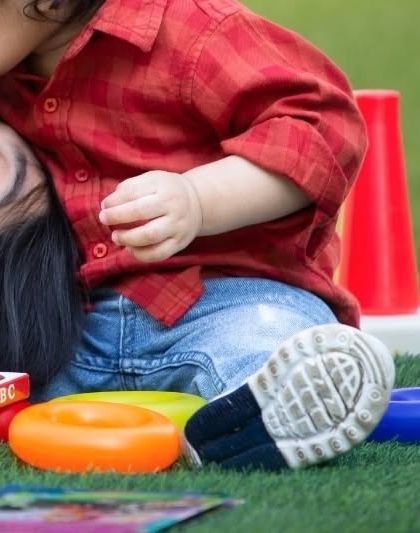 An intimate, close-up photo of a baby kissing his mother's head while they play on the grass. A beautiful detail shot that speaks volumes about their bond.