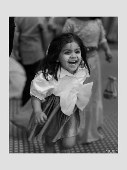 A candid black and white photo of a young girl running and laughing, capturing the joyful and carefree spirit of a wedding.