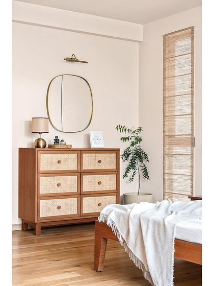On the other side of the master bedroom, a chest of drawers with rattan fronts maintains the design harmony. Brass accents and banana fiber blinds add layers of texture and earthy charm.