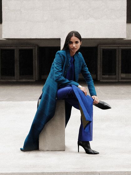 A full-length look in a brilliant royal blue. The styling is monochromatic and layered, creating a striking visual against the neutral grey concrete.