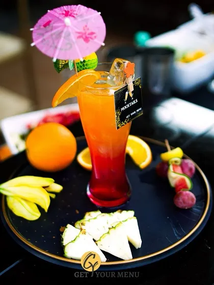 A classic layered mocktail with orange and grenadine, garnished with a fruit skewer and a fun umbrella. A tropical delight for all ages.