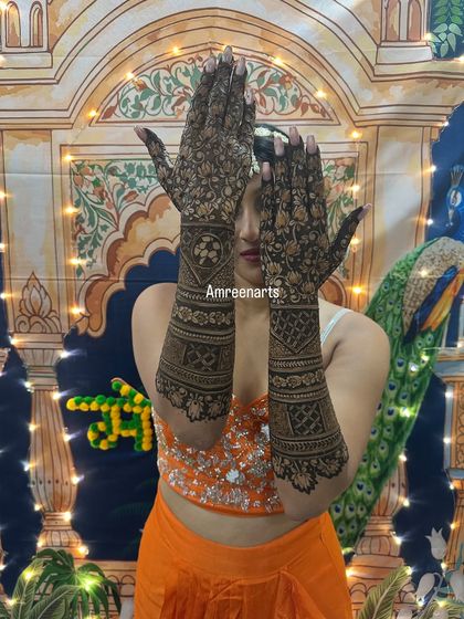 A bride playfully showing off her full-coverage mehndi, with dense, intricate patterns covering her hands and arms.
