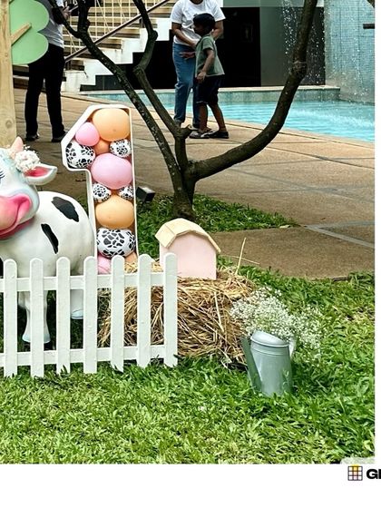 A life-sized cow prop stands by a hay bale and a balloon-filled number '1', perfect for a farm-themed first birthday.