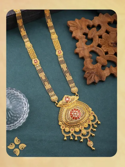 This gold mangalsutra is a cherished symbol of love. The large, ornate pendant with red enamel work makes it a statement piece that is both traditional and beautiful.