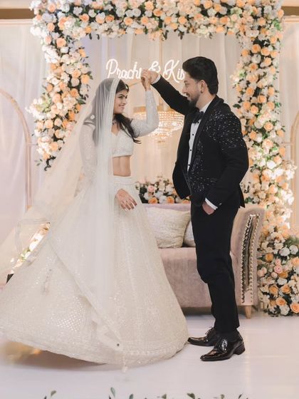 The couple shares a dance at their engagement party. Dressed in a stunning white lehenga and a black tuxedo, they look like they're in a fairytale.