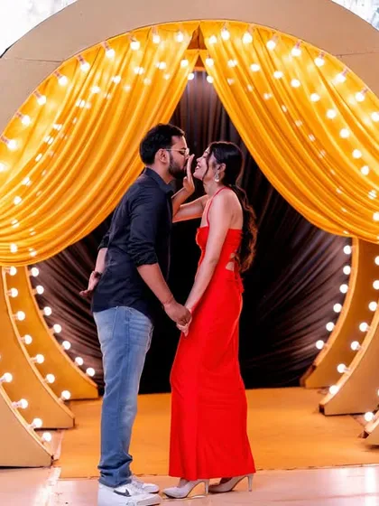 A romantic kiss in front of a stage-like setup with golden curtains and lights.