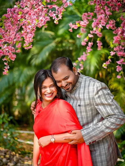An embrace filled with laughter and warmth, framed by beautiful pink blossoms. This candid pre-wedding photograph highlights the genuine happiness and easy connection between the couple.