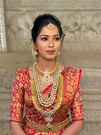 A side view of the bold red saree look, emphasizing the intricate gold jewellery and elegant updo.