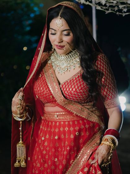 A classic bridal portrait in a traditional red lehenga. The bride's demure pose and the rich details of her attire and jewelry are beautifully captured.