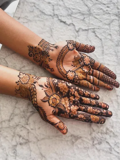 This Pinterest-inspired design combines two different styles. One hand has a large floral vine pattern, while the other features a crescent moon shape, both popular in modern designer mehndi.