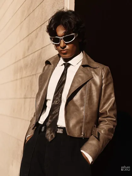 A modern take on men's fashion styling. The makeup is minimal, focusing on clean skin and defined features, while the hair is styled to have natural movement and texture, complementing the edgy outfit.