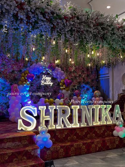 A beautiful stage setup for a first birthday, featuring a floral backdrop, marquee name, and balloon arch.