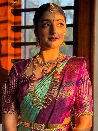 A stunning portrait of a client in a turquoise and purple Kanchivaram, with golden hour lighting highlighting her features and the custom striped blouse.