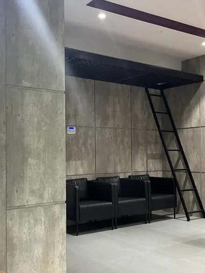 An industrial-inspired waiting area for FedEx, featuring concrete-paneled walls and a small loft space accessible by a ladder. This design choice adds a unique, functional element to the office.