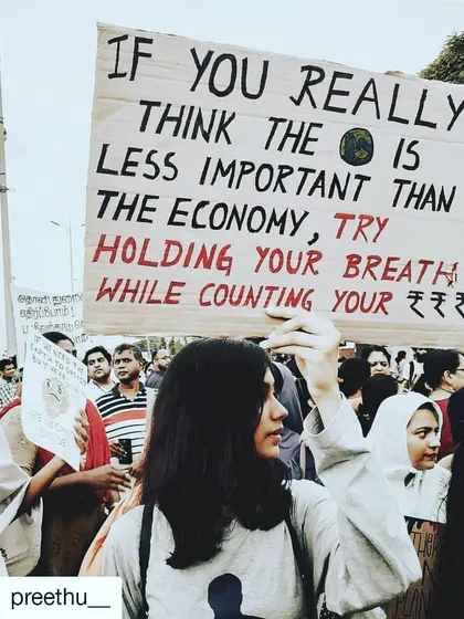 A protestor in India holds a sign that reads, "If you really think the Earth is less important than the economy, try holding your breath while counting your money." It's a sharp, witty, and profound statement on our priorities.