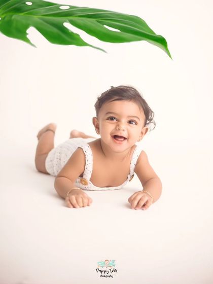 That happy baby smile is everything. A simple white background and a single green leaf are all that's needed to capture this joyful moment.