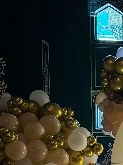 A detail shot of the balloon arrangement against the venue's dark, patterned wall. The contrast of the gold and white balloons creates a dramatic and luxurious effect.