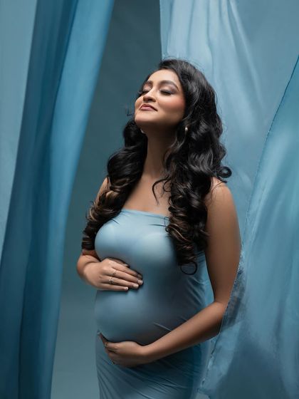 A soft and dreamy portrait surrounded by waves of blue fabric. This shot focuses on the mother's peaceful expression as she connects with her baby.