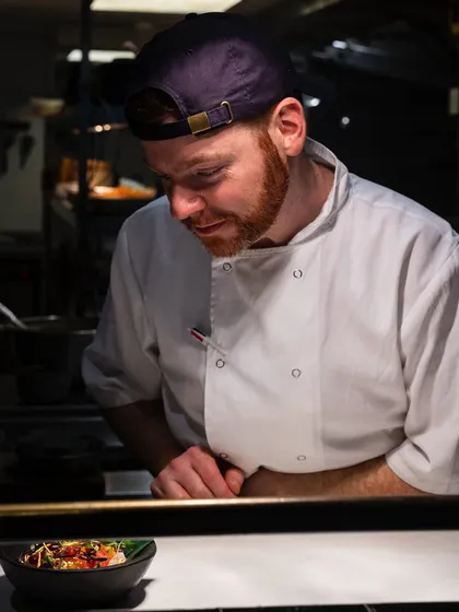 A portrait of a chef intently focused on plating a dish. This image puts a face to the food, highlighting the professionalism and concentration in a high-end kitchen.