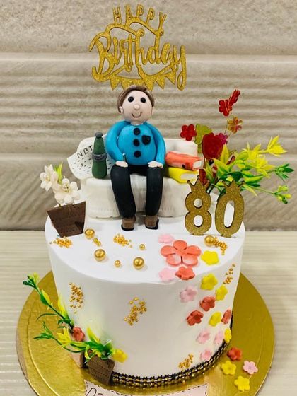 Celebrating 80 strong years with this personalized cake. It features a custom fondant figure relaxing on a sofa, surrounded by colorful flowers, marking a life well-lived.