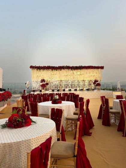 A wide shot of the rooftop reception area, with tables dressed in white and rich red. The stunning stage in the background creates a beautiful and cohesive look for this wedding at The Orchid Hotel.